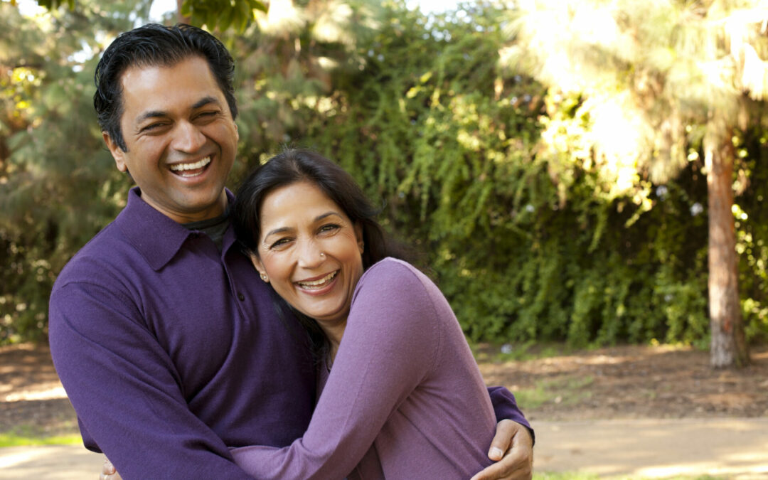Smiling man and woman, both wearing purple, hugging outside